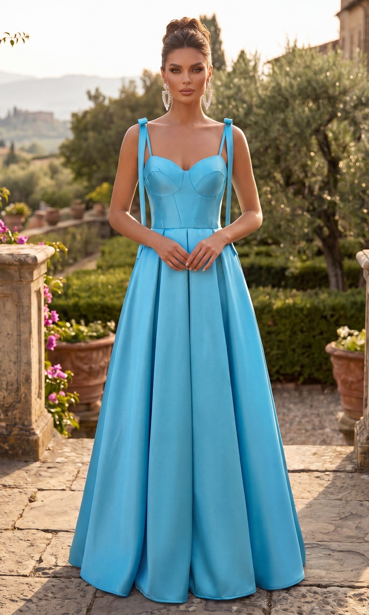 A woman wearing the Long Prom Dress: Chicas DM8033 in blue, featuring a long A-line silhouette with straps and a sweetheart neckline, stands outdoors on a stone path surrounded by greenery and landscape.